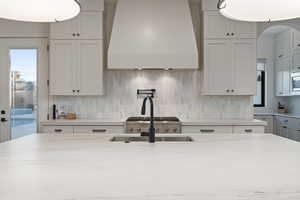 Kitchen featuring white cabinetry, decorative backsplash, custom exhaust hood, and light stone countertops