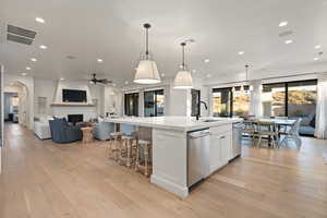 Kitchen featuring a spacious island, sink, white cabinetry, decorative light fixtures, and stainless steel dishwasher