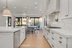 Kitchen featuring hanging light fixtures, premium range hood, sink, and white cabinets