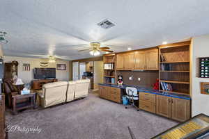 Office area featuring ceiling fan, built in desk, light carpet, and a textured ceiling