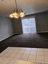 Tiled spare room with carpet floors, baseboards, a chandelier, and visible vents