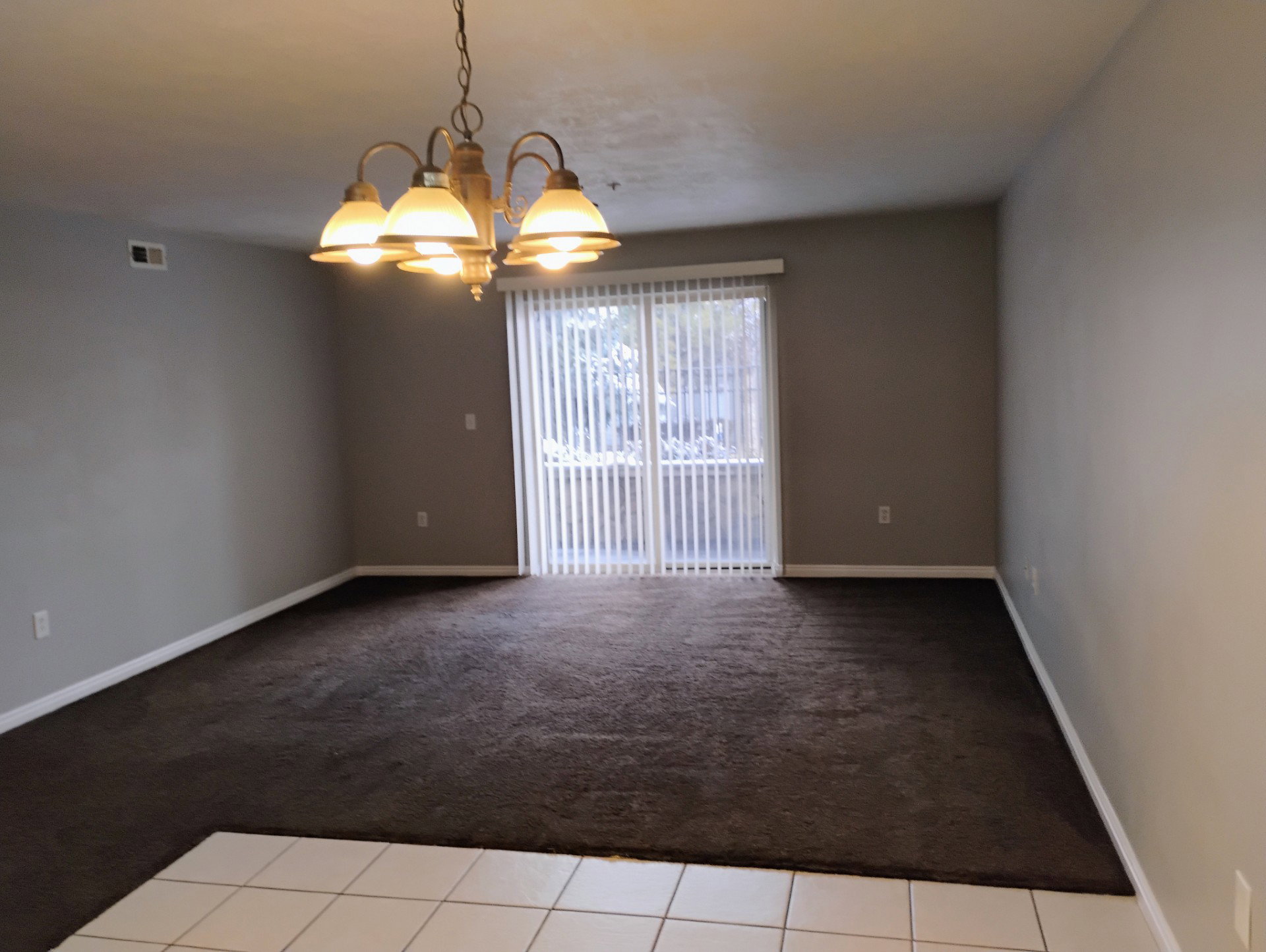 Carpeted empty room with baseboards, a notable chandelier, visible vents, and tile patterned floors