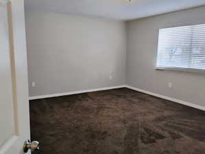 Empty room with baseboards and dark carpet