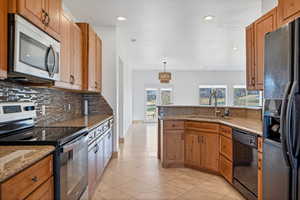 Kitchen with pendant lighting, tasteful backsplash, sink, black appliances, and light stone countertops