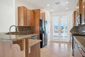 Kitchen featuring light tile patterned floors, backsplash, stainless steel appliances, light stone counters, and kitchen peninsula