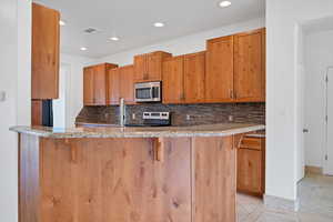 Kitchen with appliances with stainless steel finishes, a breakfast bar, decorative backsplash, and kitchen peninsula