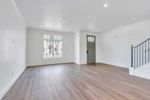 Unfurnished living room featuring stairs, baseboards, light wood-type flooring, and ornamental molding