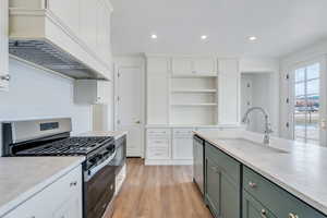 Kitchen with custom range hood, a sink, open shelves, appliances with stainless steel finishes, and white cabinets