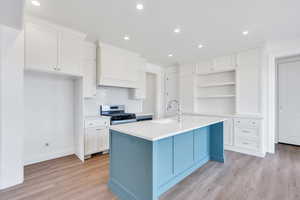 Kitchen featuring light wood-type flooring, a sink, open shelves, white cabinets, and stainless steel gas range