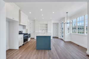 Kitchen with open shelves, stainless steel gas range, an inviting chandelier, white cabinetry, and a sink