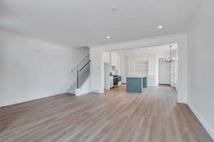 Unfurnished living room with ornamental molding, a sink, an inviting chandelier, light wood finished floors, and stairs