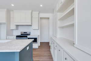 Kitchen with open shelves, white cabinets, light countertops, built in microwave, and stainless steel gas range