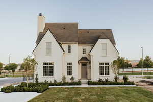 View of front of home with a front yard, a chimney, stucco siding, and roof with shingles