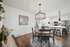 Dining area with dark hardwood / wood-style flooring, sink, wooden walls, and a chandelier