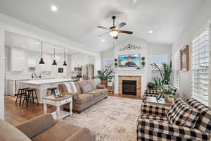 Living room featuring sink, a tile fireplace, ceiling fan, light hardwood / wood-style floors, and vaulted ceiling