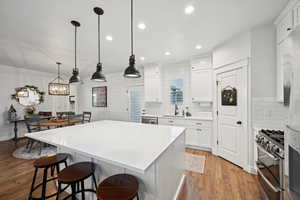 Kitchen with hardwood / wood-style flooring, appliances with stainless steel finishes, white cabinetry, hanging light fixtures, and backsplash