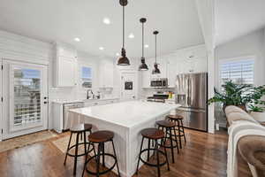 Kitchen with hanging light fixtures, stainless steel appliances, white cabinets, and a kitchen island