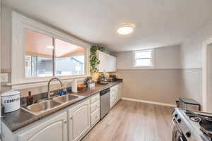 Kitchen with sink, range, light hardwood / wood-style floors, white cabinets, and stainless steel dishwasher