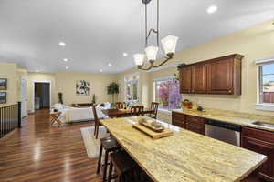 Kitchen with decorative light fixtures, dishwasher, sink, light stone counters, and dark wood-type flooring