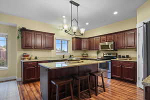 Kitchen with appliances with stainless steel finishes, decorative light fixtures, dark hardwood / wood-style flooring, a center island, and light stone countertops