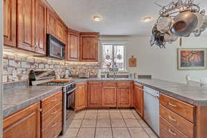 Kitchen featuring light tile patterned floors, appliances with stainless steel finishes, backsplash, tile counters, and a textured ceiling