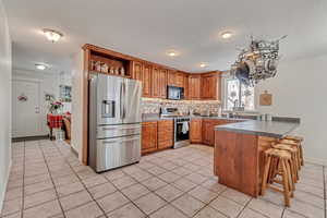 Kitchen with appliances with stainless steel finishes, backsplash, a kitchen breakfast bar, light tile patterned floors, and kitchen peninsula