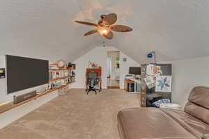 Living room featuring vaulted ceiling, light colored carpet, ceiling fan, and a textured ceiling