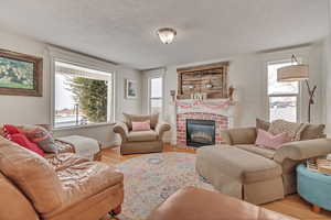 Living room with a brick fireplace, a wealth of natural light, a textured ceiling, and light hardwood / wood-style flooring