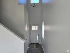 Doorway to outside with a towering ceiling, a chandelier, and dark colored carpet