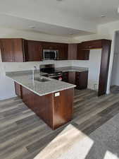 Kitchen featuring appliances with stainless steel finishes, wood-type flooring, sink, dark brown cabinetry, and kitchen peninsula