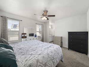 Carpeted bedroom featuring ceiling fan, connected bathroom, multiple windows, and a textured ceiling