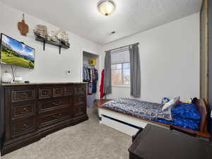 Bedroom with light carpet, a closet, and a textured ceiling