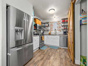 Kitchen with sink, light hardwood / wood-style flooring, white cabinetry, stainless steel appliances, and a textured ceiling