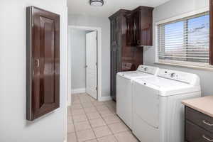 Main-floor laundry room featuring cabinets, light tile patterned flooring, and washing machine and clothes dryer