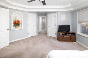 Bedroom with a raised ceiling, ornamental molding, light colored carpet, and ceiling fan