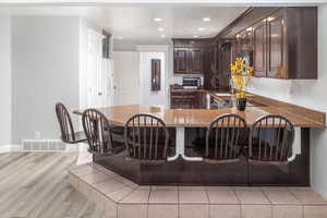 Kitchen with light wood-type flooring, sink, dark brown cabinetry, and kitchen peninsula