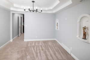 Dining area with a raised ceiling, light colored carpet, and a notable chandelier