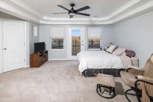 Bedroom with ceiling fan, a tray ceiling, access to exterior balcony, and light carpet