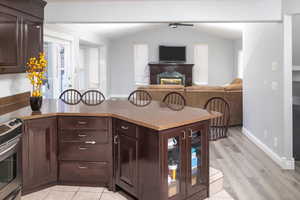 Kitchen with light wood-type LVP flooring, dark brown cabinets, vaulted ceiling, and stainless steel electric range oven