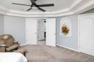 Bedroom featuring a raised ceiling, crown molding, light colored carpet, and ceiling fan