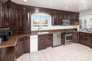 Kitchen featuring light tile patterned flooring, sink, dark brown cabinets, a textured ceiling, and appliances with stainless steel finishes