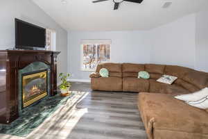 Living room with hardwood / wood-style flooring, ceiling fan, lofted ceiling, and a high end fireplace