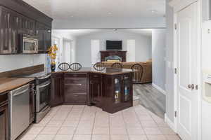 Kitchen featuring stainless steel appliances, light tile patterned flooring, lofted ceiling, and dark brown cabinetry