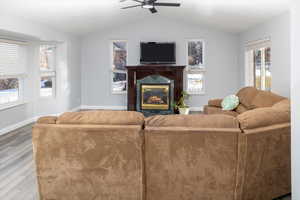 Living room featuring ceiling fan, wood-type flooring, a fireplace, and vaulted ceiling