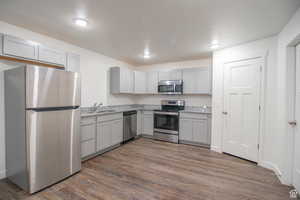 Kitchen with sink, gray cabinetry, stainless steel appliances, light stone countertops, and dark hardwood / wood-style flooring