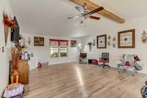 Living area with ceiling fan, light hardwood / wood-style floors, lofted ceiling with beams, and a textured ceiling