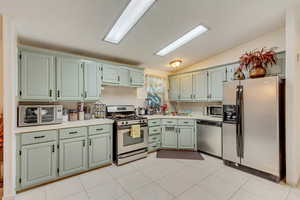 Kitchen with stainless steel appliances, light tile patterned flooring, lofted ceiling, and sink