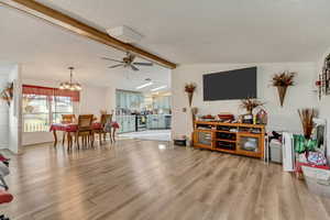 Living room featuring ceiling fan with notable chandelier, light hardwood / wood-style floors, a textured ceiling, and vaulted ceiling with beams