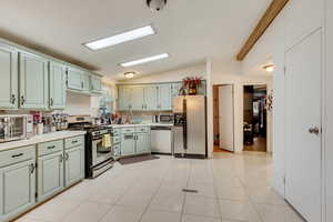 Kitchen featuring appliances with stainless steel finishes, sink, light tile patterned floors, and lofted ceiling