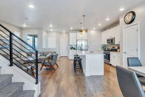 Kitchen featuring white cabinetry, appliances with stainless steel finishes, a kitchen island with sink, and hanging light fixtures